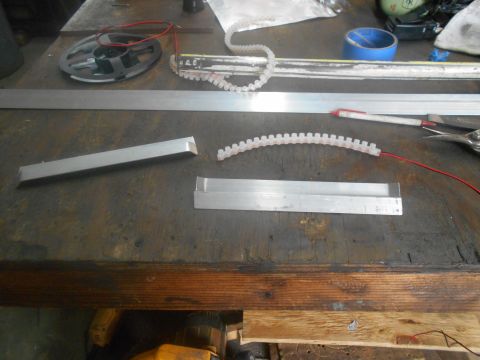 1992 Ford Bronco - A workbench scene with various metal parts, a spool of wire, and a flexible white plastic strip with red wires attached. A blue tape roll a…