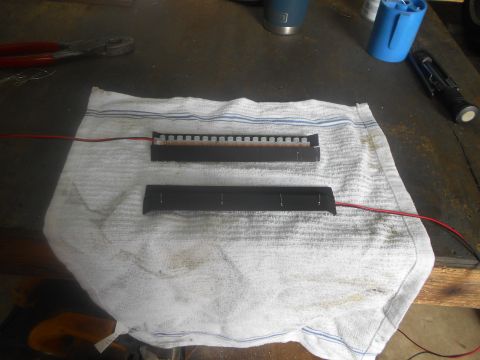 1992 Ford Bronco - Two black strips with electrical components are laid out on a white towel on a workbench. One strip has a row of small, square components,…