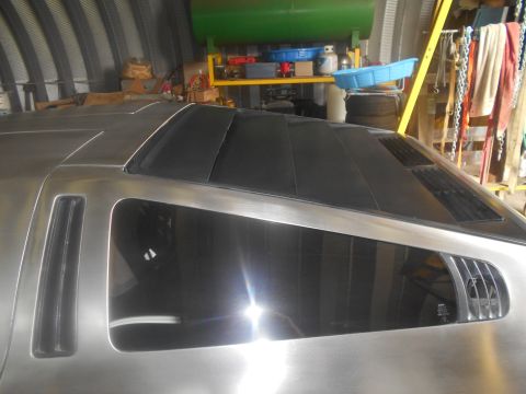 1992 Ford Bronco - The rear quarter panel and roof of a custom vehicle with a brushed metal finish and tinted windows are shown in a workshop setting. Visible…