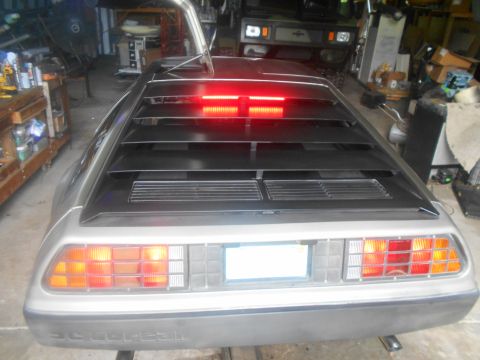 1992 Ford Bronco - The rear of a silver DeLorean DMC-12 is shown in a garage setting. The car has its rear louvers and brake lights illuminated.