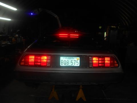 1992 Ford Bronco - Rear view of a silver DeLorean DMC-12 with its gullwing doors open, illuminated by red taillights and a blue light above the driver's side…
