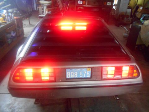 1992 Ford Bronco - The rear of a DeLorean DMC-12 with its iconic red taillights illuminated. The car has a Florida license plate reading BQ8 575.