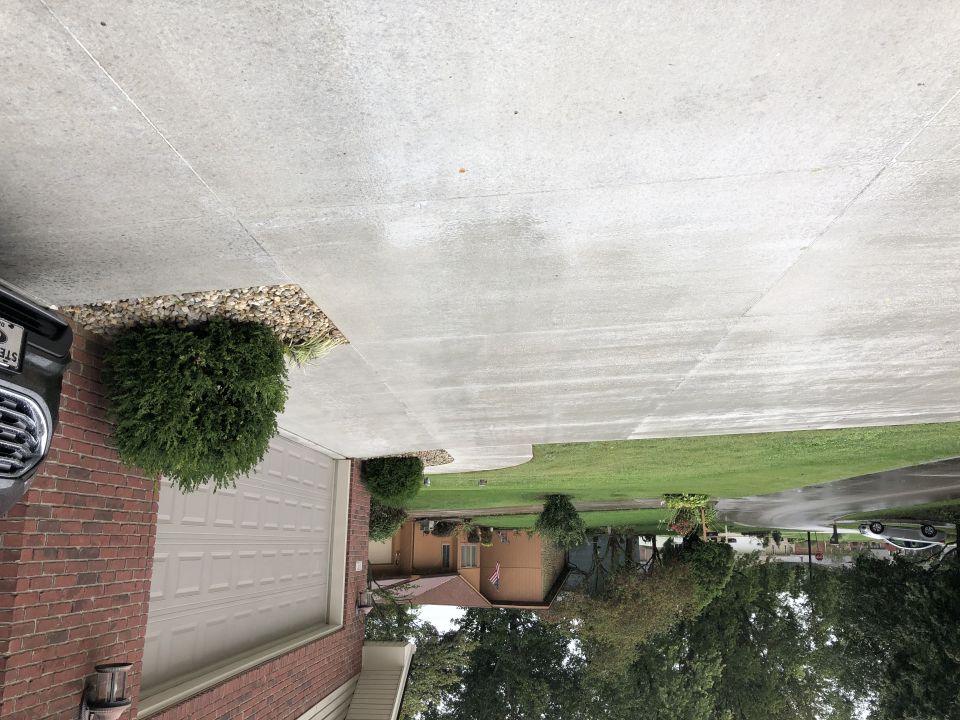 Partial view of a dark vehicle in a driveway next to a brick garage.