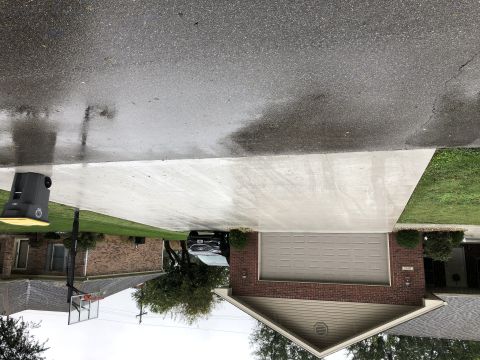 1995 Mercury Grand Marquis - A black sedan is parked in a driveway next to a brick house with a garage. The driveway is wet, suggesting it has recently rained.