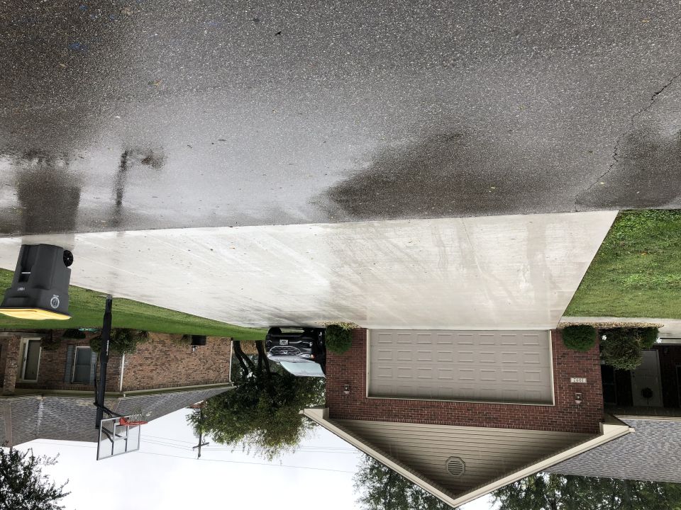 Black sedan parked in a wet driveway next to a brick house.