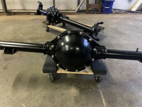 1979 Jeep CJ5 - Two black painted rear axle assemblies are shown in a workshop setting. The front axle assembly is in focus, resting on a wooden dolly with…