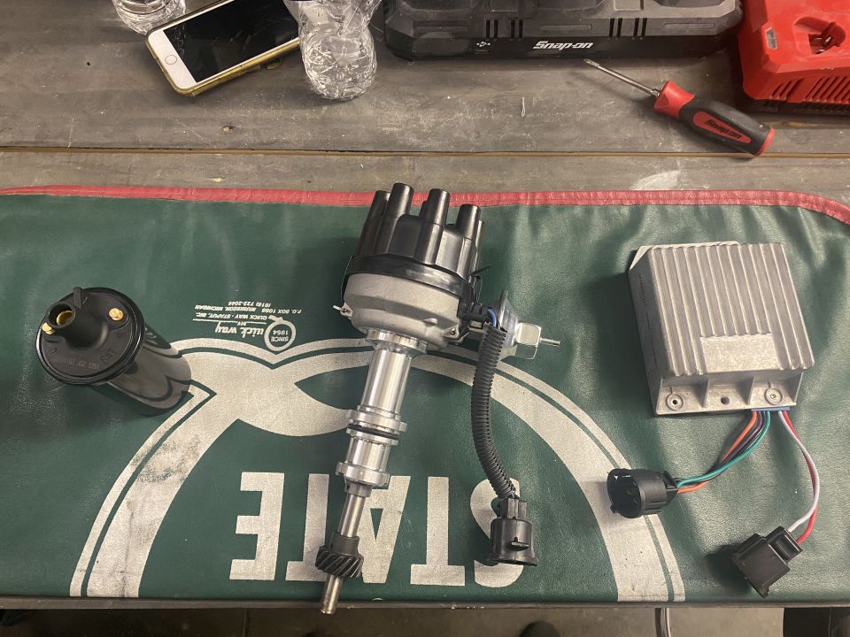 Automotive ignition parts including a distributor, coil, and control module on a green mat.