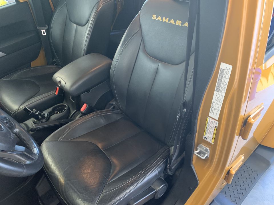 Black leather interior of a Jeep Wrangler Sahara with gold logo on passenger seat.