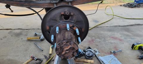 1996 Ford Bronco - A close-up view of a rusty rear axle hub and brake drum assembly, likely from a 1996 Ford Bronco, with several tools scattered on the concr…