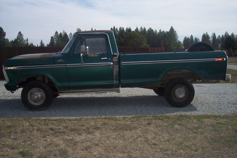 Green 1977 Ford F-150 pickup truck, side view, with rust on hood and fender, spare tire in bed