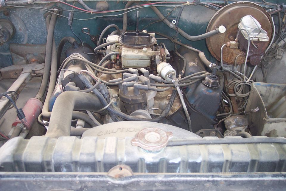 Engine bay with carburetor, distributor, and radiator visible. 'CAUTION' text on fan shroud