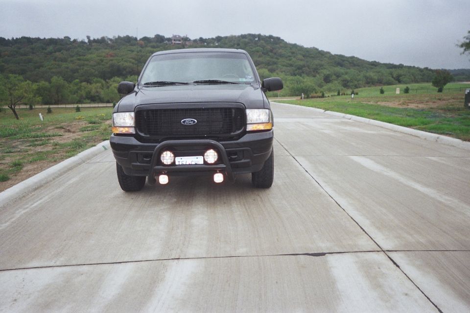 Black Ford Excursion SUV front view with brush guard and driving lights on concrete road