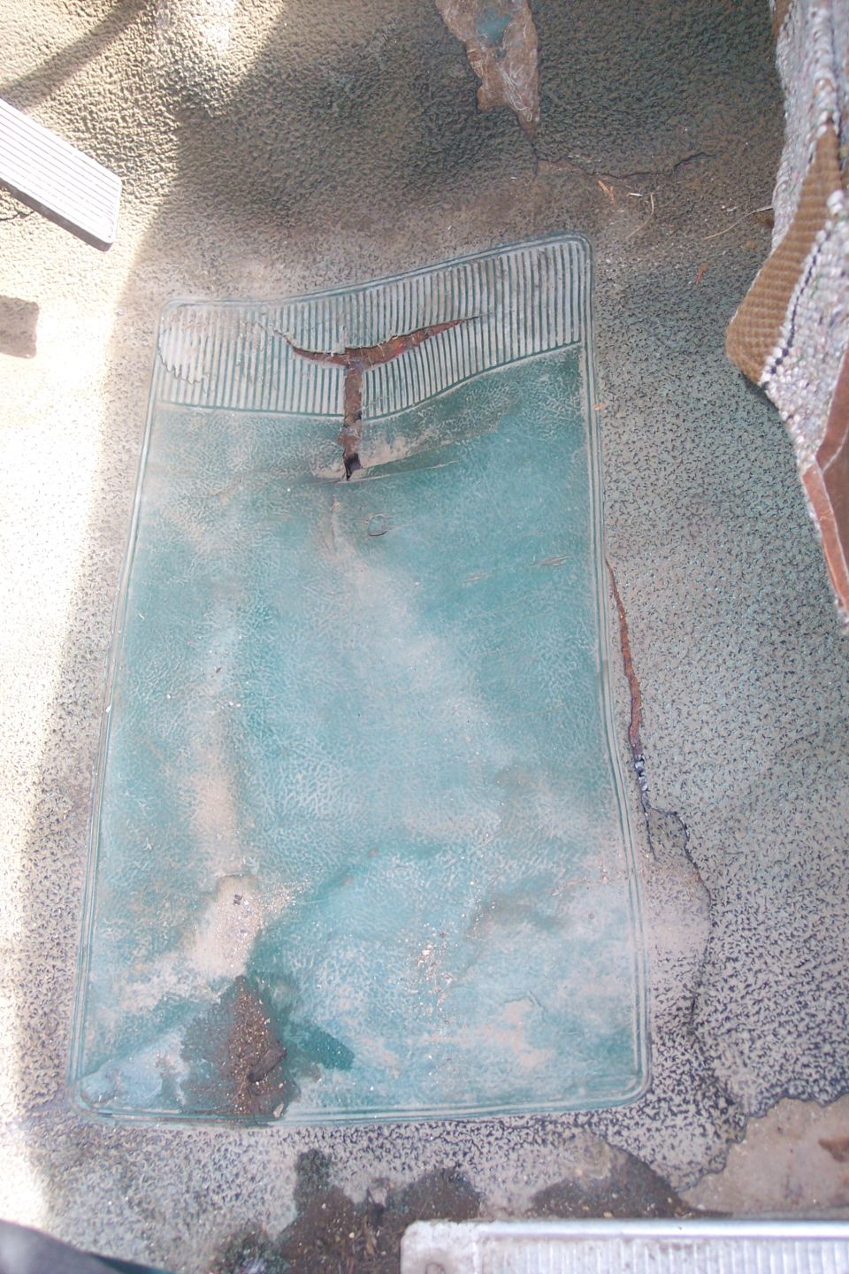 worn teal floor mat with a metal piece sticking out of a tear