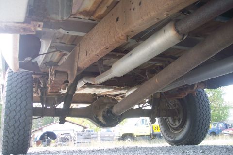 1977 Ford F-150 - The undercarriage of a pickup truck reveals its exhaust system and rear axle, with other vehicles in the background.
