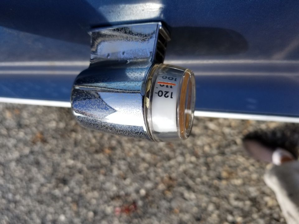 Close-up of a chrome-plated exterior temperature gauge on a blue car, showing markings for 100, 110, and 120 degrees
