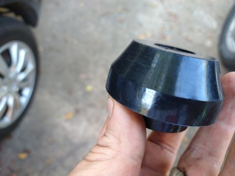 1996 Ford Bronco - A close-up of a suspension bushing is held in a hand, with a vehicle's wheel visible to the left.