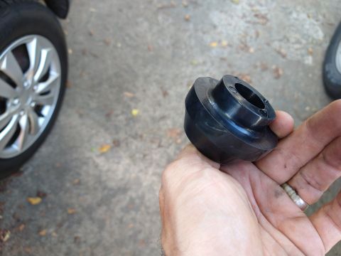 1996 Ford Bronco - A hand holds a black rubber bushing with a metal insert in front of a portion of a silver car wheel and tire.