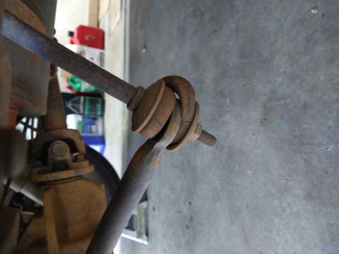 1996 Ford Bronco - A close-up view of a rusty sway bar end link assembly on a vehicle. The assembly connects to a suspension component with a threaded bolt an…