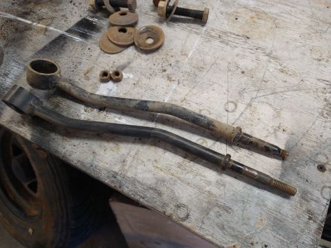 1996 Ford Bronco - Two rusty control arms are laid out on a weathered wooden workbench next to some washers and nuts. A tire is visible on the left side of th…