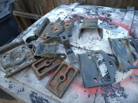 1996 Ford Bronco - A collection of rusted and worn metal brackets and parts are laid out on a surface with red and white spray paint splatters. The parts appe…