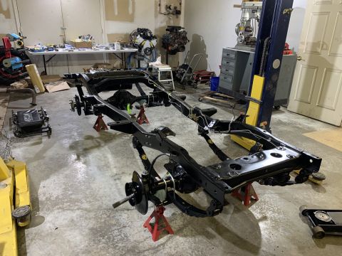 1979 Jeep CJ5 - A black Jeep CJ5 frame is elevated on red jack stands in a garage setting. Various tools and vehicle parts are visible in the background.