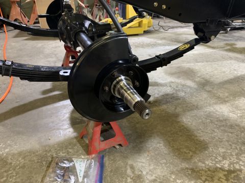 1979 Jeep CJ5 - A close-up view of a vehicle's front axle assembly, featuring leaf springs, a brake rotor, and a splined hub, all painted black and support…