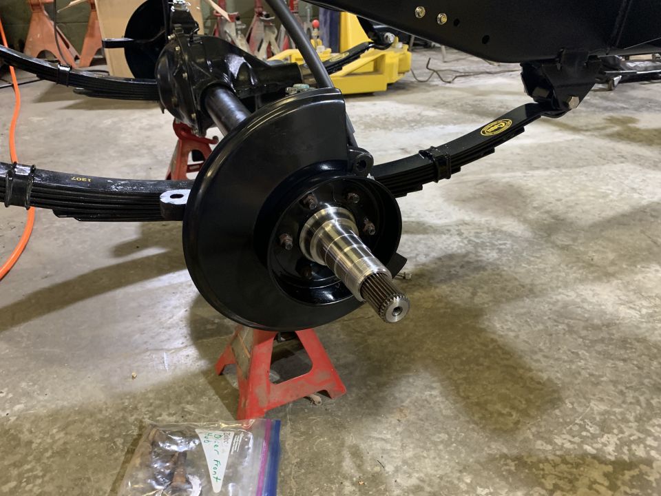 Close-up of a black front axle assembly with leaf springs, brake rotor, and hub.