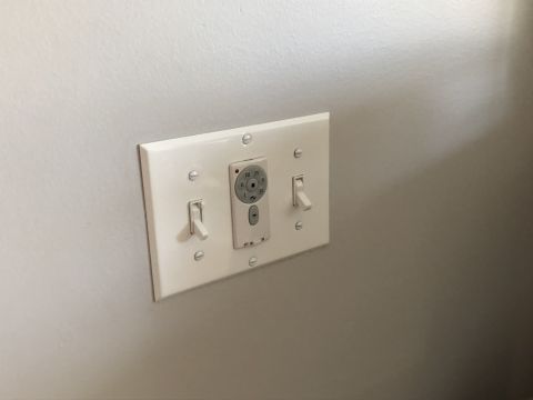 1995 Mercury Grand Marquis - A white wall plate with two light switches and a fan speed controller is mounted on a gray wall.