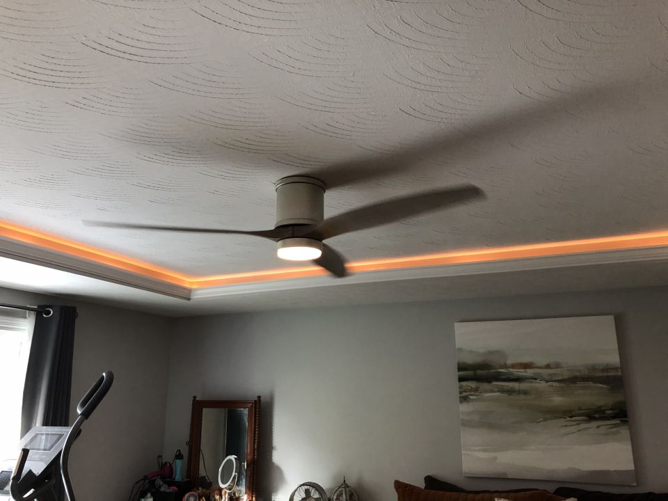 Ceiling fan with orange LED lighting, textured ceiling, and abstract painting.