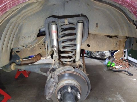 1996 Ford Bronco - The rear suspension of a red vehicle is shown, featuring a large coil spring, shock absorber, brake rotor, and caliper. The vehicle is supp…