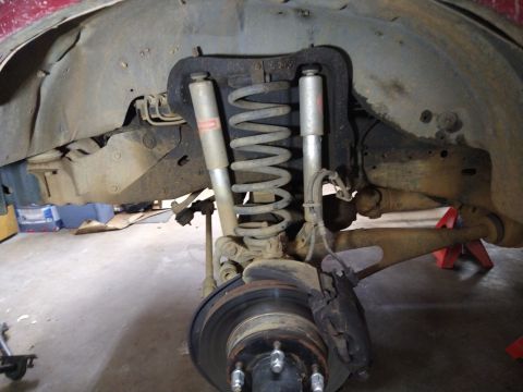 1996 Ford Bronco - The rear suspension of a red 1996 Ford Bronco is shown, with the coil spring, shock absorber, brake rotor, and caliper clearly visible. The…