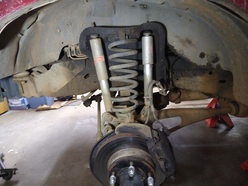 1996 Ford Bronco rear suspension with coil spring, shock, brake rotor, caliper, raised on jack stands.