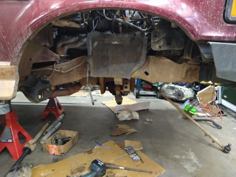 1996 Ford Bronco - The front driver's side suspension and undercarriage of a red Ford Bronco are visible, supported by red jack stands. Various automotive par…