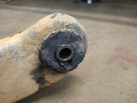 1996 Ford Bronco - A close-up view of a worn and cracked rubber bushing with a metal insert, attached to a dirty, rust-colored metal suspension component.