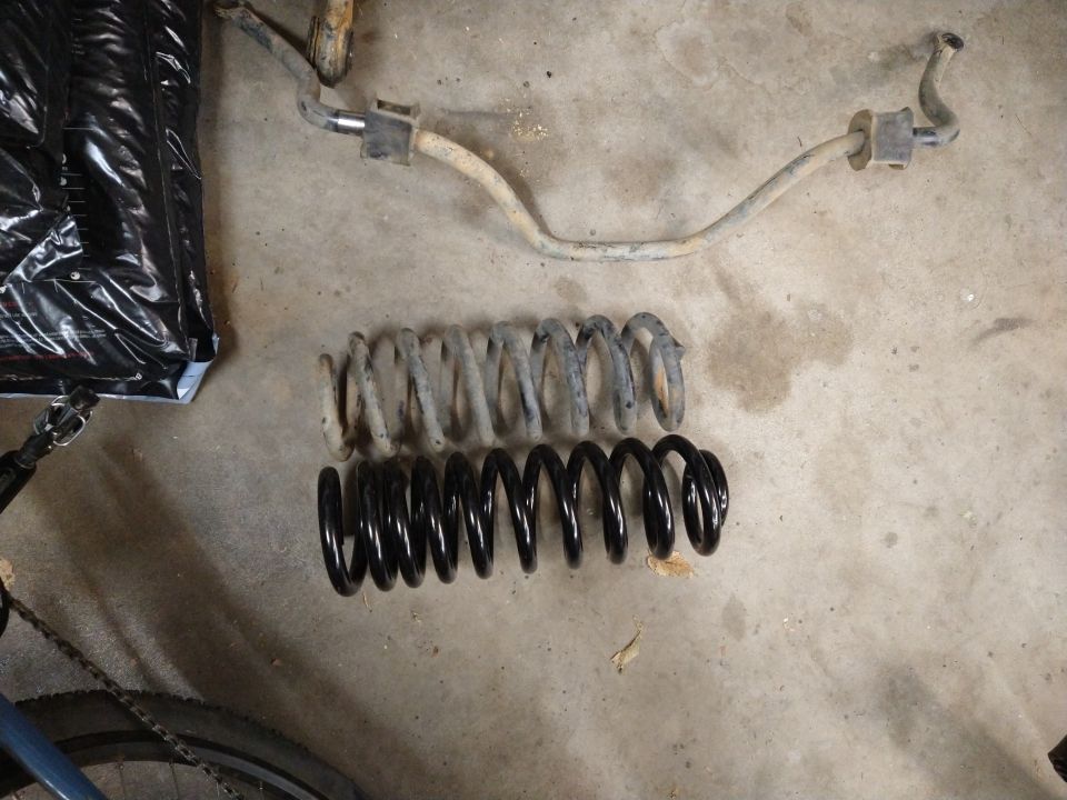 Old rusty sway bar and two coil springs, one old and one new black one