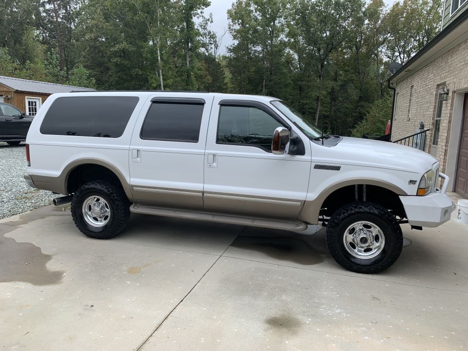White Ford Excursion with tan trim, tinted windows, and chrome wheels parked on a driveway.