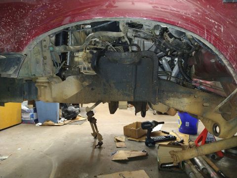 1996 Ford Bronco - The underside of a red Ford Bronco's wheel well is shown, with the suspension and engine components exposed. Tools and parts are scattered…