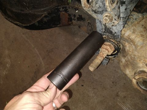 1996 Ford Bronco - A hand holds a dark-colored socket wrench extension near a rusty bolt and bracket on what appears to be a vehicle's suspension component. T…