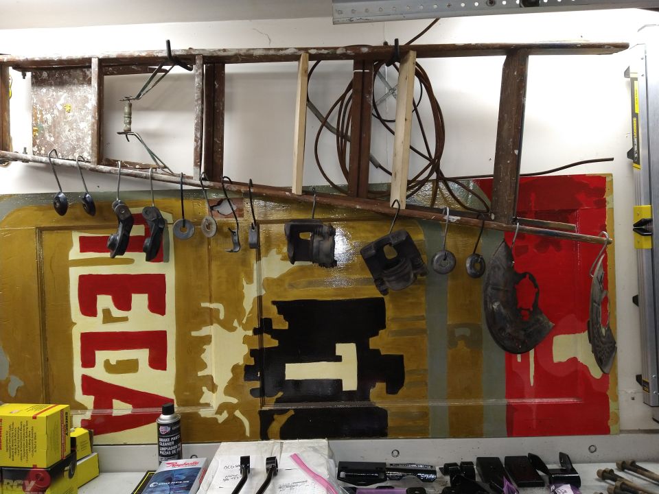 Automotive parts and a painted door displayed on a workbench and hung from a ladder.