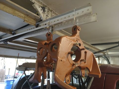 1996 Ford Bronco - Two large, rust-colored metal automotive parts are hanging from chains attached to a ceiling track. The parts appear to be suspension compo…