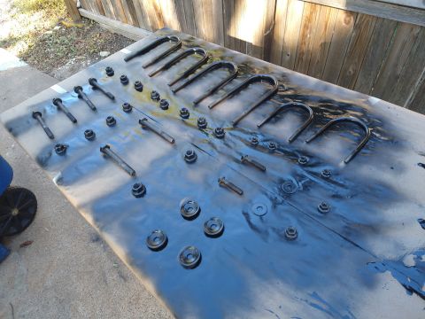 1996 Ford Bronco - Several U-bolts and bolts with nuts are laid out on a surface covered with black spray paint, suggesting preparation for a project.