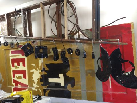 1996 Ford Bronco - Several black automotive brake caliper parts and rotor dust shields are hanging from hooks on a wooden rod, suspended in front of a painted…