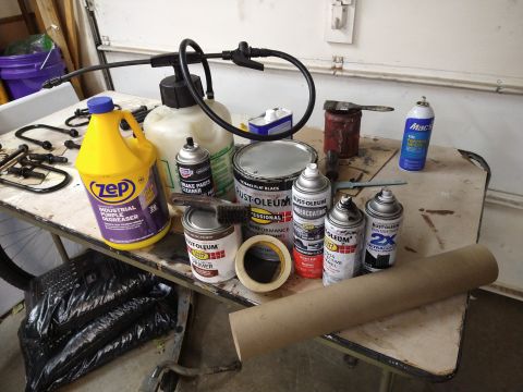 1996 Ford Bronco - A collection of automotive maintenance and painting supplies are laid out on a workbench. Items include various cans of spray paint and cle…