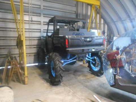 1992 Ford Bronco - A black Can-Am UTV with large, aggressive tires and blue suspension components is parked inside a metal building. A portion of a clear bubb…