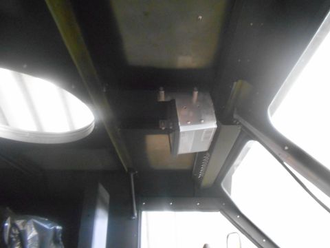 1992 Ford Bronco - Interior view of a vehicle's ceiling, showing a metal bracket with a silver box mounted to it. A circular opening with a white surface is v…