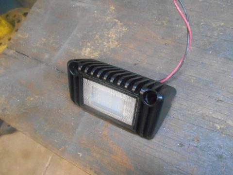 1992 Ford Bronco - A black LED light with red and black wires is resting on a wooden surface. The light has a ribbed casing and a clear lens with visible LEDs.