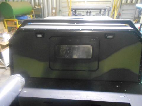 1992 Ford Bronco - The rear of a custom vehicle with camouflage paint is shown in a workshop setting. A rectangular window is visible in the center of the rea…