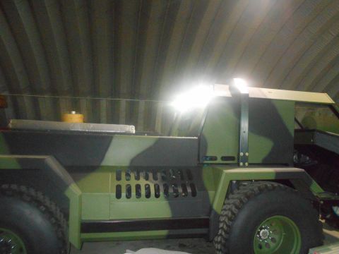 1992 Ford Bronco - A camouflaged vehicle, possibly a custom build, is parked indoors under a corrugated metal ceiling. The vehicle features large tires, a rug…