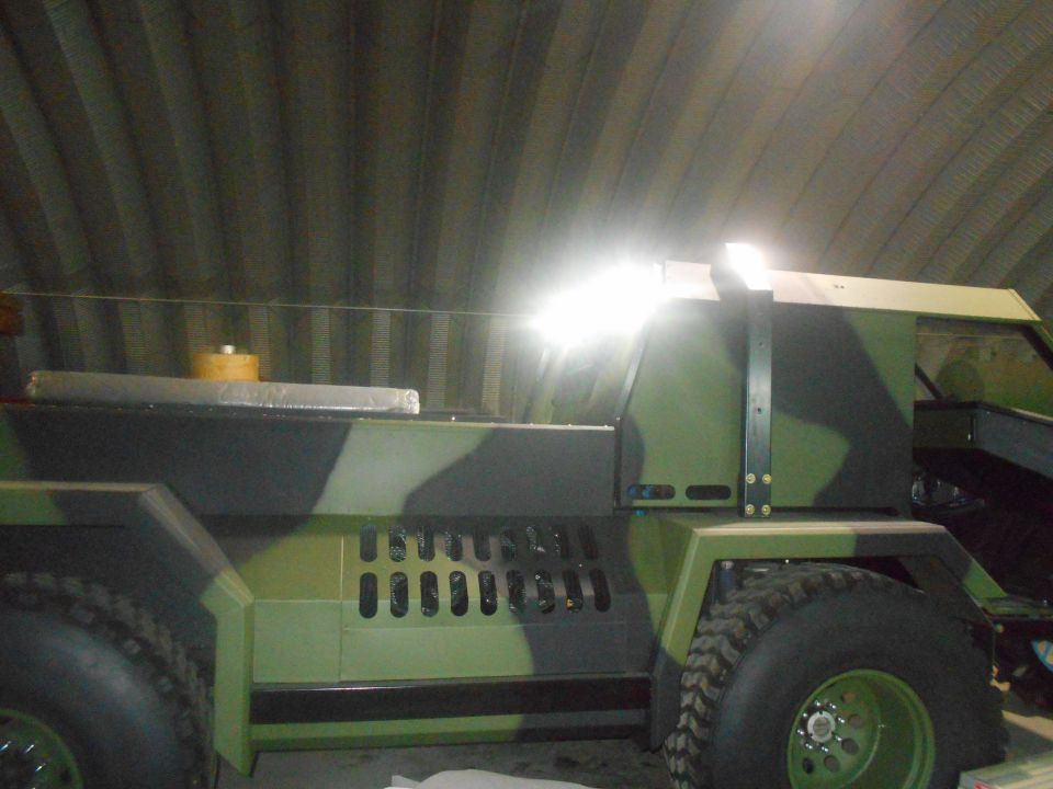 Camouflaged custom vehicle with large tires parked indoors.