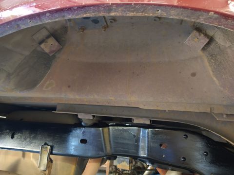 1996 Ford Bronco - The underside of a vehicle shows the wheel well area with some rust and a newly painted black frame rail. Metal brackets are visible in the…